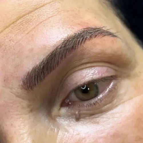 Primer plano del ojo de una persona con una ceja arqueada y rellena. La piel se ve lisa y el ojo mira ligeramente hacia arriba.