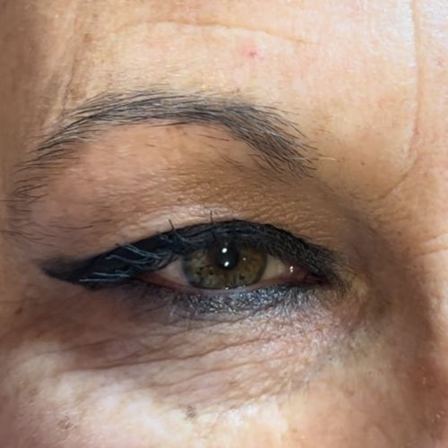 Primer plano del ojo de una persona con delineador negro y vello mínimo en las cejas, mostrando algunas arrugas alrededor del área de los ojos.