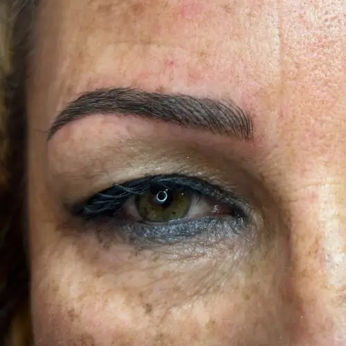 Primer plano del ojo de una persona con delineador azul, ceja definida y algo de textura de piel y pecas visibles.