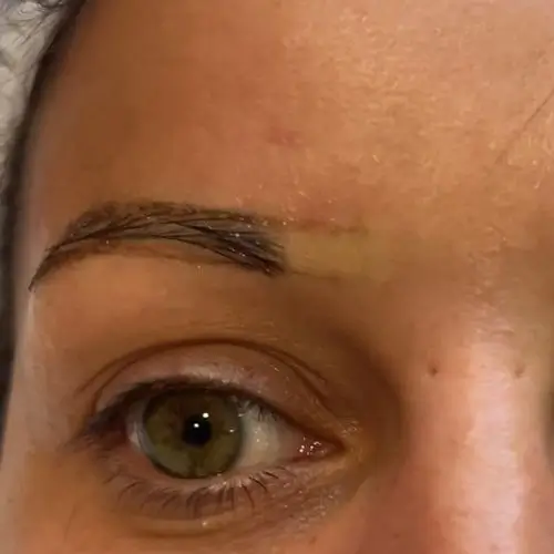Primer plano del ojo derecho de una persona que muestra una ceja parcialmente aplicada o descolorida con algo de maquillaje o tatuaje visible en la piel.