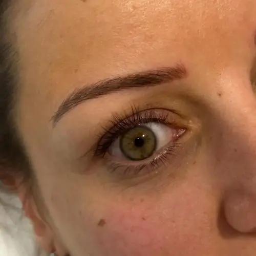 Un primer plano del ojo de una persona con una ceja arqueada, iris marrón, pestañas largas y un lunar en la mejilla.