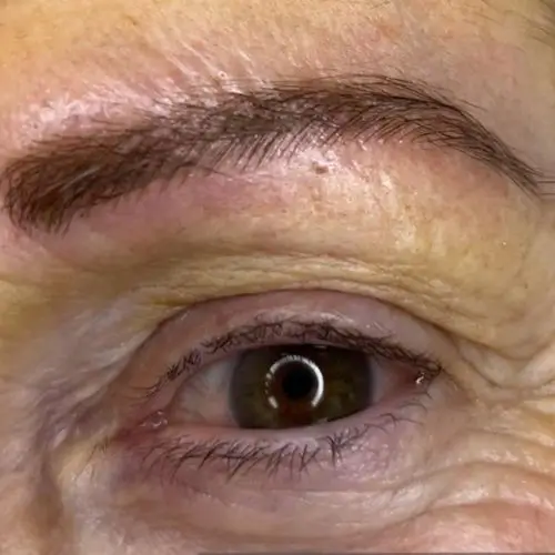 Primer plano del ojo de una persona que muestra la textura detallada de la piel, arrugas y una ceja visible.